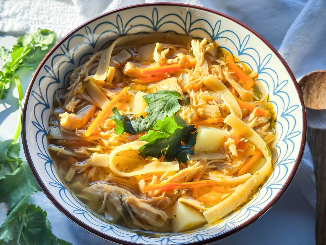 A close-up photo of a bowl of chicken noodle soup with shredded chicken and herbs